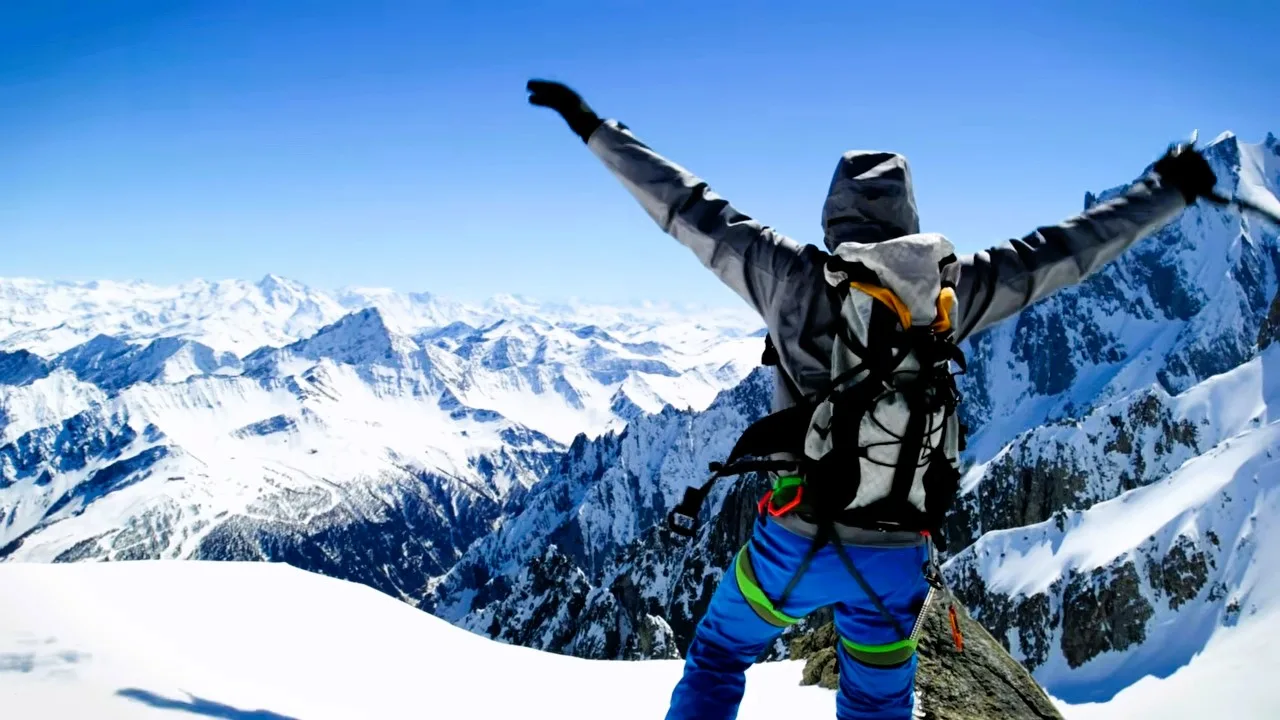 Trekker with arms raised on a snowy summit facing Himalayan peaks