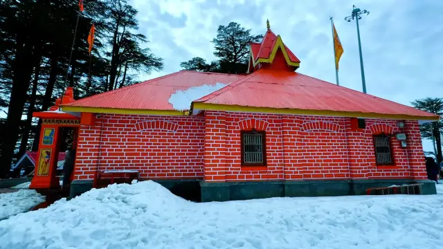 Red-roofed Himachali temple surrounded by snow and deodar trees