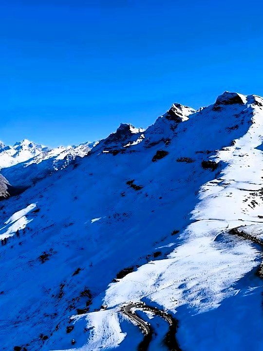 Snow-covered mountain ridge and winding road above Manali