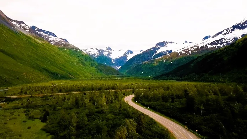 Winding road through a green valley below snowy peaks in Himachal Pradesh