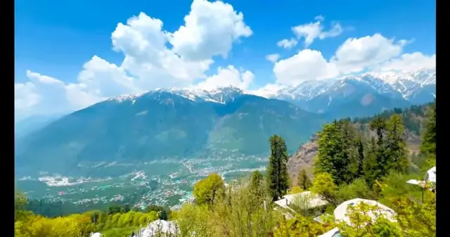 Green valley town below snow-capped peaks under a blue sky in Himachal