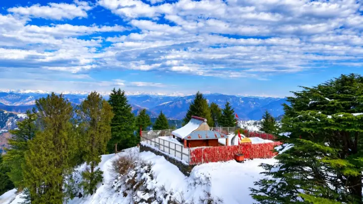 Snow-covered Nag Devta temple at Mahasu Peak in Kufri with Himalayan peaks behind