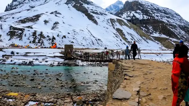 Small wooden footbridge over a river with snowy banks and mountains near Manali