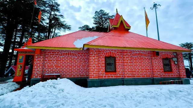 Red-roofed Himachali temple surrounded by snow and deodar trees