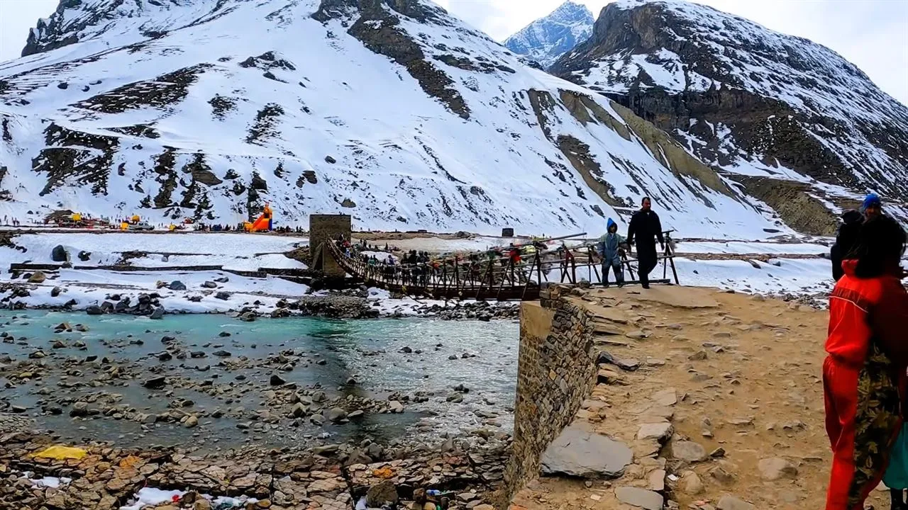 Footbridge over a glacial river below snowy peaks near Manali