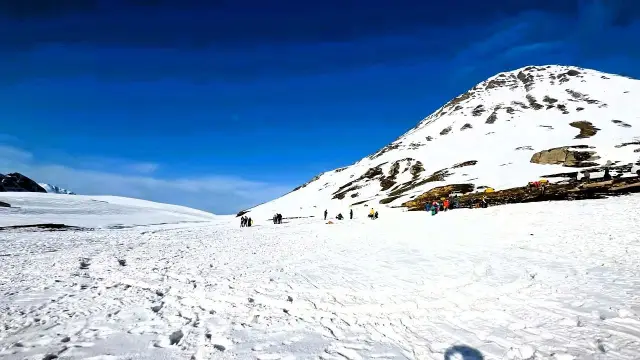 Visitors walking across a wide snowfield below a snow-covered hill