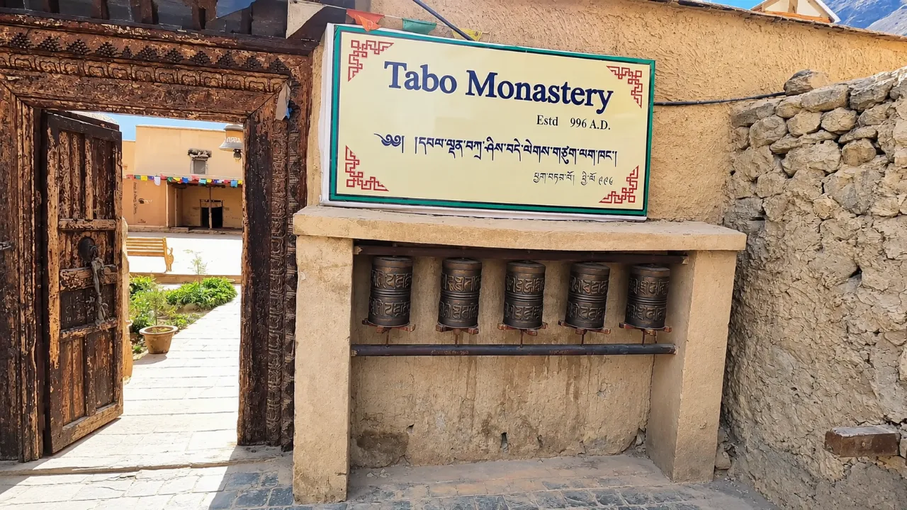 Tabo Monastery entrance sign, established 996 AD, with prayer wheels and a carved wooden gate in Spiti